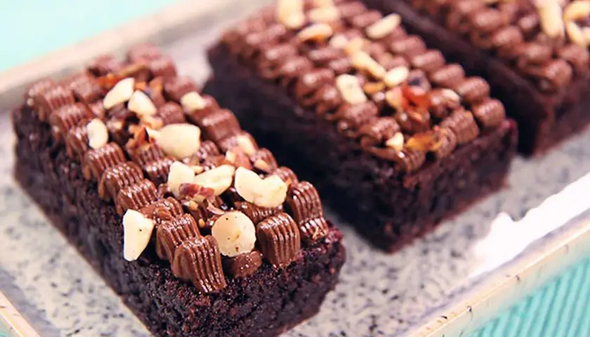 Mörka, saftiga glutenfri brownie bitar toppade med chokladfrosting och nötter på ett marmorerat fat.