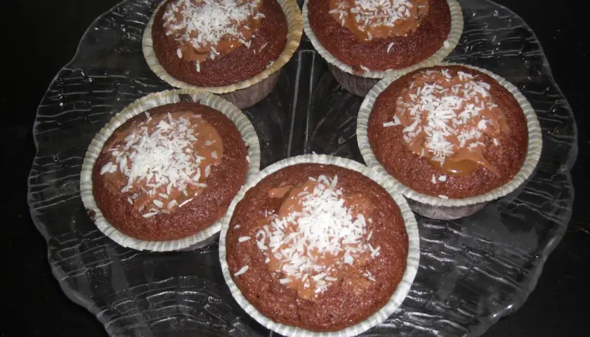 Fem kladdkakemuffins med kola och kokosflingor på ett glasfat.