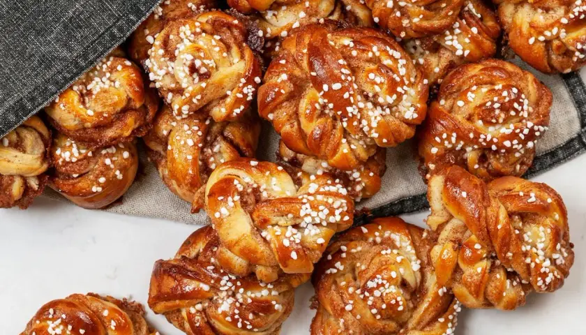 En hög med gyllene snurra bullar, toppade med pärlsocker. Doften av kanel sprider sig från dessa nybakade godsaker.