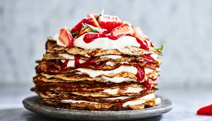 En imponerande pannkakstårta med grädde och jordgubbar, perfekt för ett somrigt pannkakstårta recept.