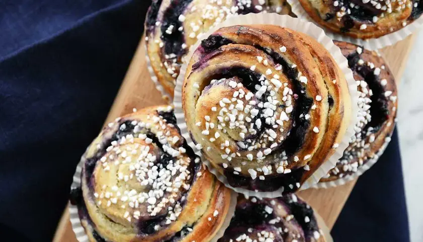 Nybakade blåbärsbullar med pärlsocker på en träbricka, redo att avnjutas.