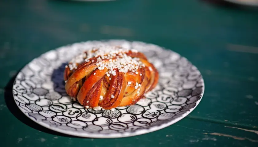 En gyllene kanelbulle med pärlsocker på en mönstrad tallrik. Perfekt för fika, kanske inspirerad av ett enkelt kanelbullar recept.