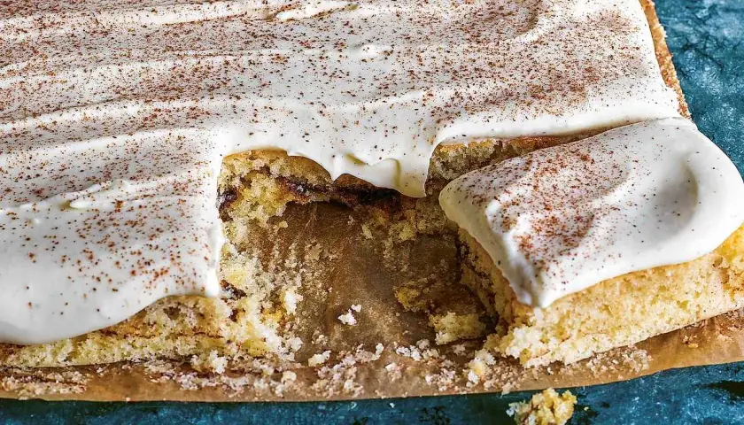 En saftig sockerkaka med krämig glasyr och ett generöst strössel av kanel. En bit saknas, redo att avnjutas.