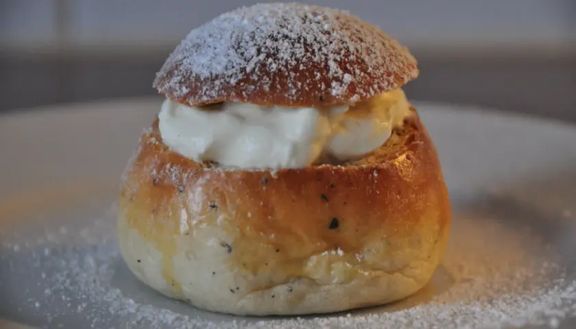 En nybakad semla, redo att avnjutas. Den gyllene bullen är fylld med fluffig grädde och pudrad med florsocker. Perfekt för att baka semmelbullar.