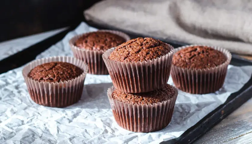 Fem choklad cupcakes i pappersformar, staplade och utspridda på vitt papper.