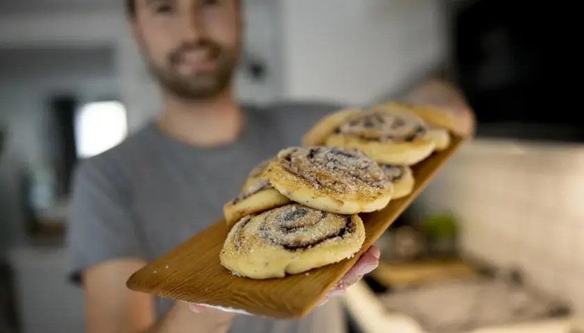 Man håller fram en bricka med nybakade kanelbullar utan ägg, strösslade med socker.