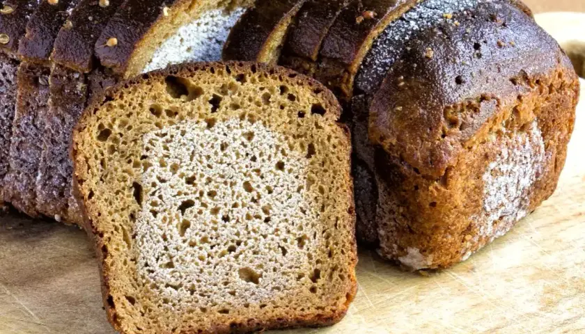 Mörkt, saftigt rågbröd skuret i skivor. En skiva ligger framför ett helt bröd. Frågan är om man kan frysa bröd två gånger.