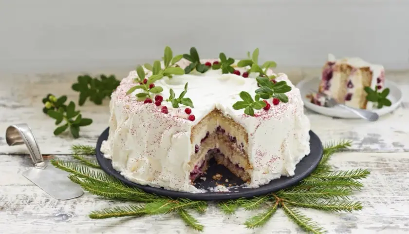 En vacker tårta med grädde, lingon och gröna kvistar. Perfekt att baka till festen!