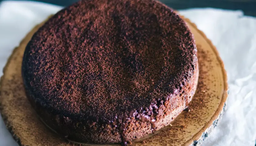 En saftig glutenfri chokladkaka, pudrad med kakao och med smält choklad som rinner ner längs kanten.
