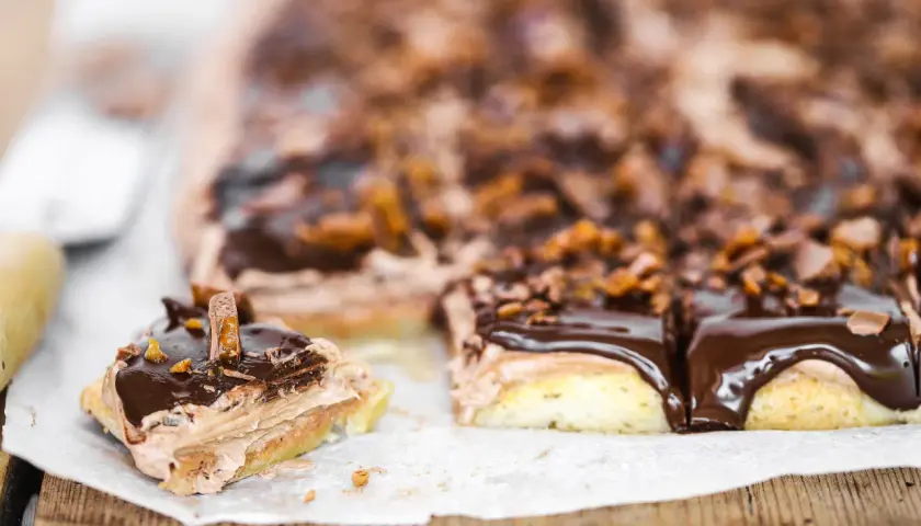 Mäktiga mjuka kakor i långpanna med chokladglasyr och krispiga bitar. En bit är uppskuren och visar lager av fluffig kräm.