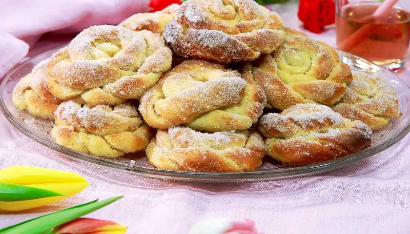 En tallrik med nybakade bullar, perfekt för att doppa bullar i socker. Tulpaner och en glas dryck i bakgrunden.