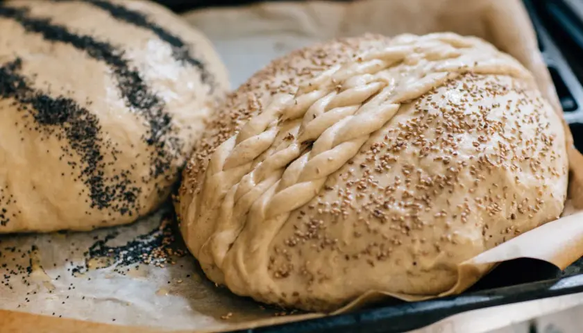 Två hembakade bröd, ett med vallmofrön och ett flätat med sesamfrön, redo att baka och frysa in.