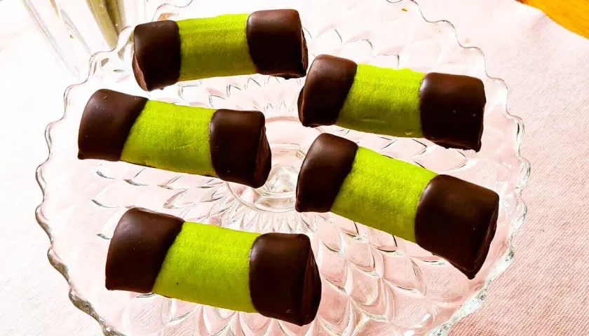Fem gröna punschrullar med chokladtoppar på ett glasfat. Perfekt för ett enkelt punschrulle recept.
