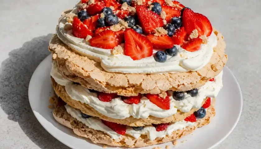 En härlig glutenfri pinocchiotårta med marängbottnar, vispad grädde och färska bär som jordgubbar och blåbär.