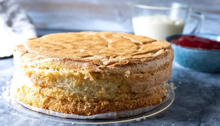 En fluffig sockerkaksbotten, redo att bli en del av ett anslag recept. Bredvid står en skål med sylt och en kanna med grädde.