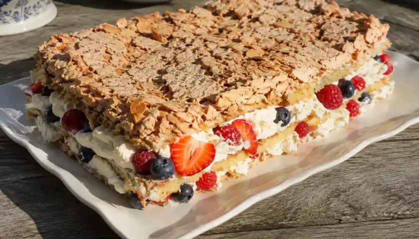 En härlig kladdkaka tårta med grädde och bär, toppad med mandel. Perfekt för sommaren!