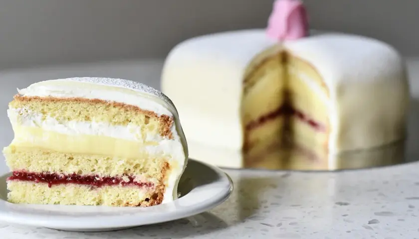 En skiva av en klassisk prinsesstårta med lager av sockerkaka, vaniljkräm, vispgrädde och hallonsylt. Perfekt för ett prinsesstårta recept.