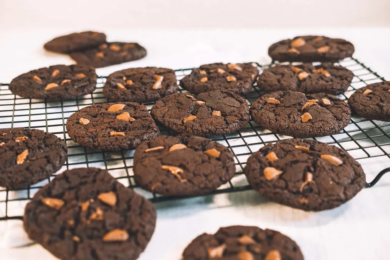 Många mörka, veganska chocolate chip cookies med chokladbitar ligger på ett svart galler.