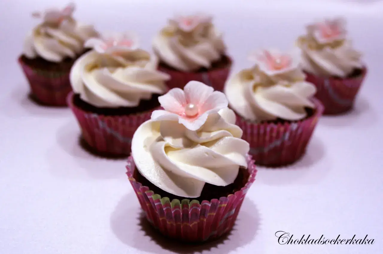 Sju små mini cupcakes med vit frosting och rosa blommor. Perfekta för ett sött kalas.