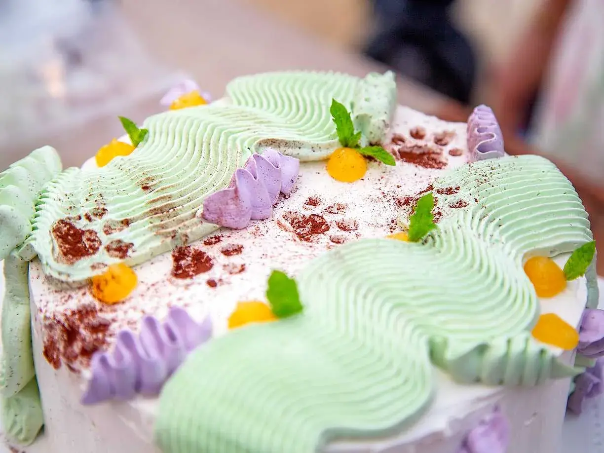 En vacker jordgubbsmousse tårta med grön och lila frosting, toppad med aprikoser och myntablad.