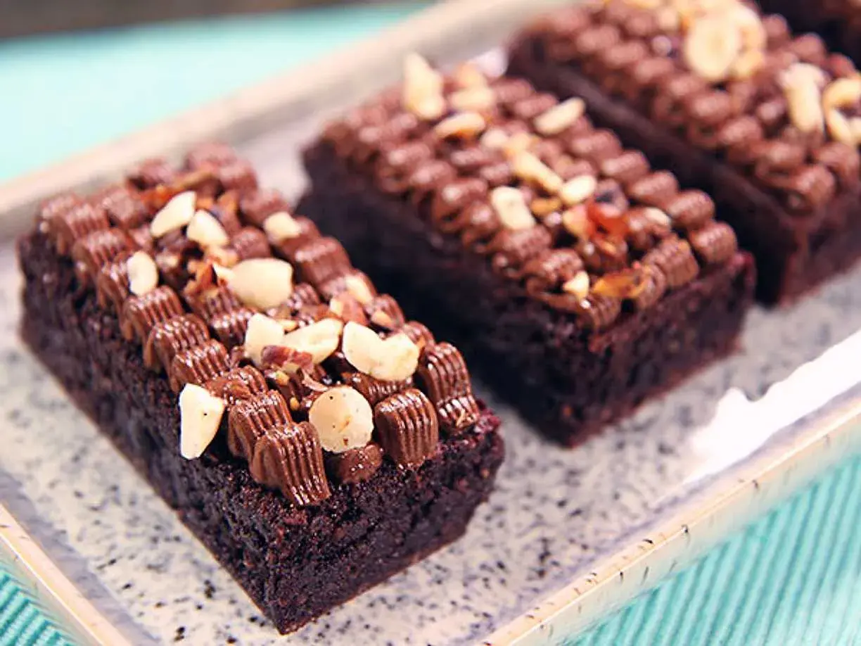 Mörka, saftiga glutenfri brownie bitar toppade med chokladfrosting och nötter på ett marmorerat fat.