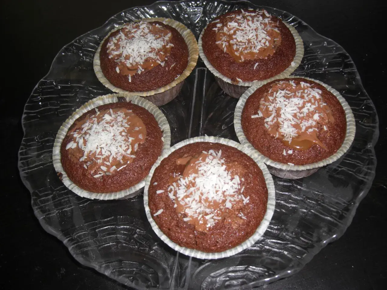 Fem kladdkakemuffins med kola och kokosflingor på ett glasfat.
