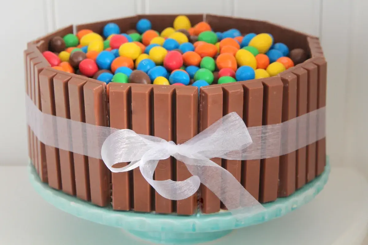 En färgglad KitKat tårta fylld med M&M's, omgiven av KitKat-bars och ett vitt sidenband. En dröm för alla godisälskare!