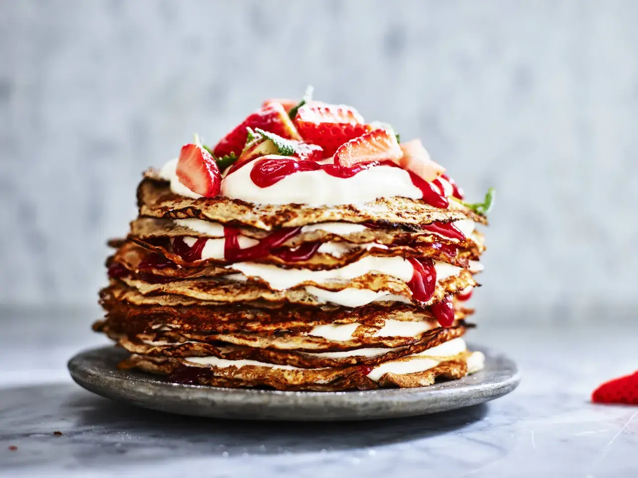 En imponerande pannkakstårta med grädde och jordgubbar, perfekt för ett somrigt pannkakstårta recept.