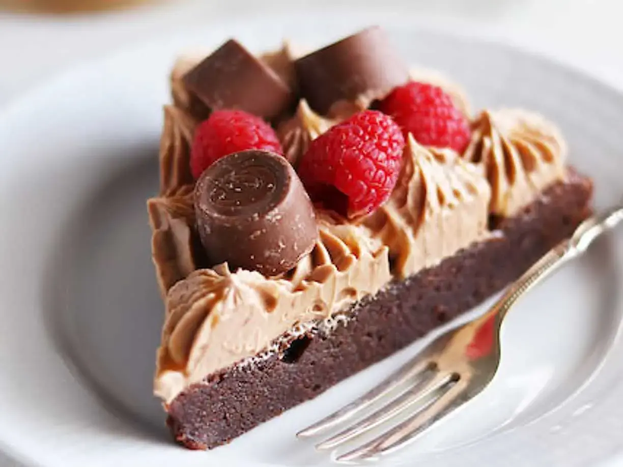 En bit kladdkaka med fluffig chokladfrosting, toppad med hallon och chokladbitar. En perfekt kombination för alla chokladälskare.