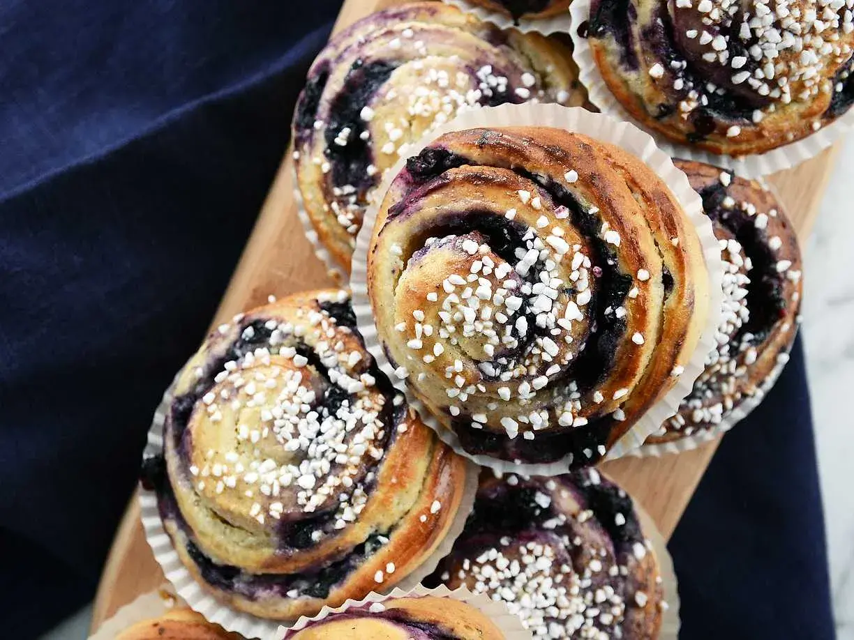 Nybakade blåbärsbullar med pärlsocker på en träbricka, redo att avnjutas.
