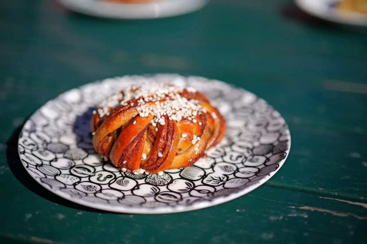 En gyllene kanelbulle med pärlsocker på en mönstrad tallrik. Perfekt för fika, kanske inspirerad av ett enkelt kanelbullar recept.