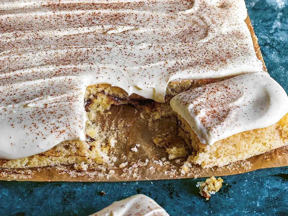 En saftig sockerkaka med krämig glasyr och ett generöst strössel av kanel. En bit saknas, redo att avnjutas.