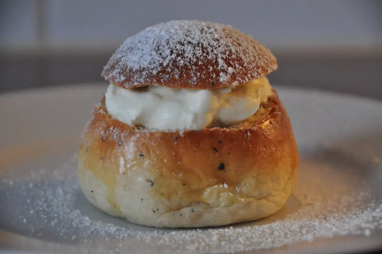 En nybakad semla, redo att avnjutas. Den gyllene bullen är fylld med fluffig grädde och pudrad med florsocker. Perfekt för att baka semmelbullar.