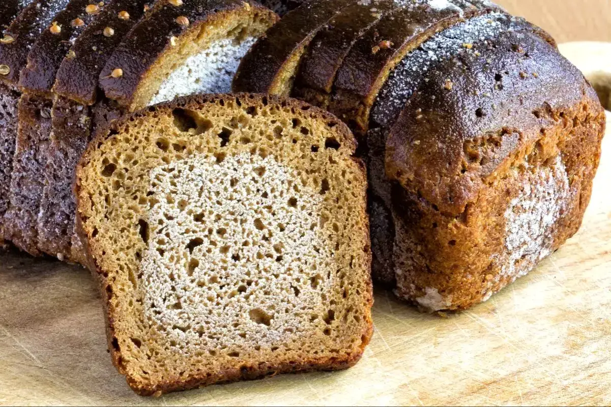 Mörkt, saftigt rågbröd skuret i skivor. En skiva ligger framför ett helt bröd. Frågan är om man kan frysa bröd två gånger.