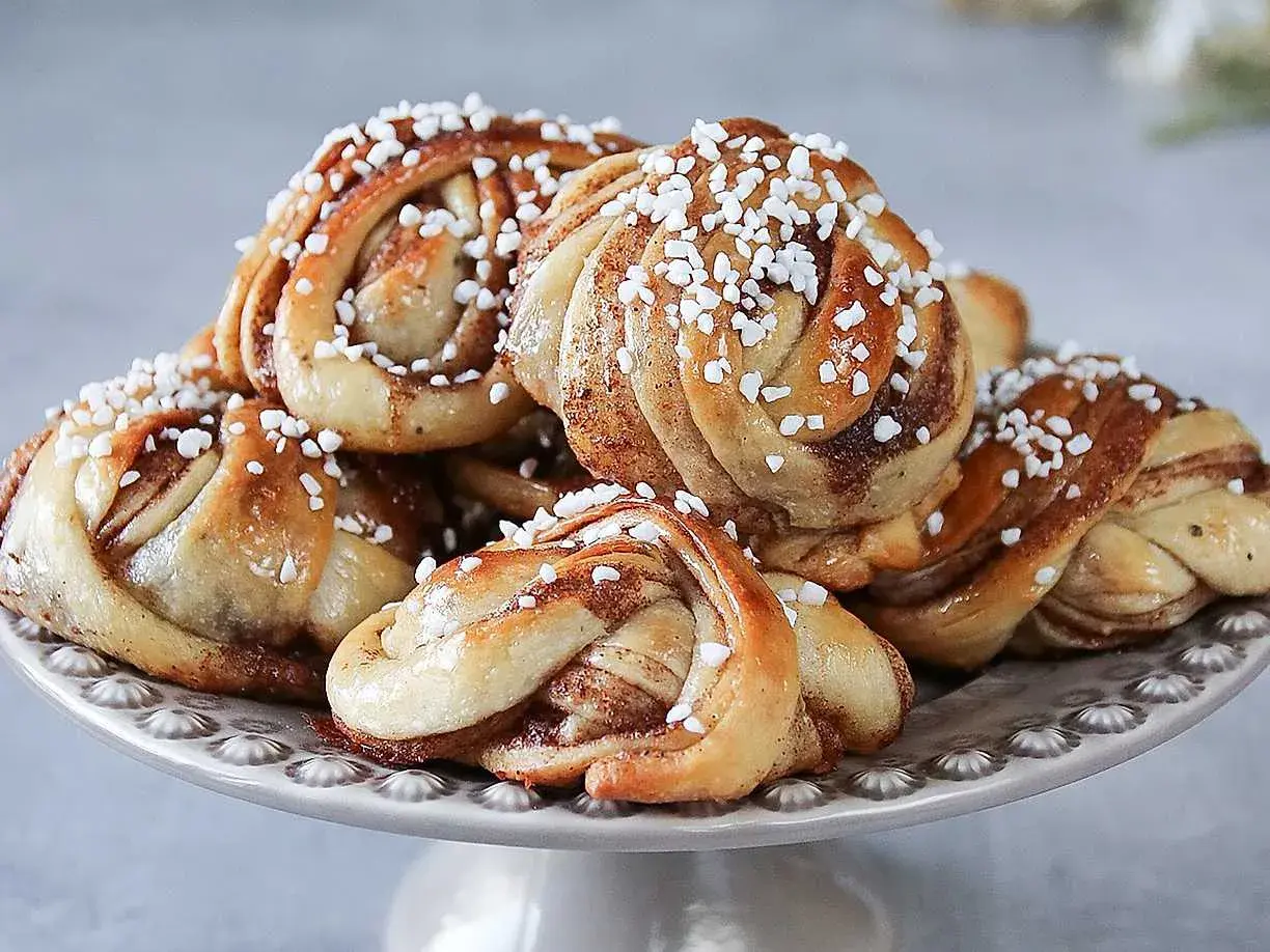 En hög med laktosfria kanelbullar, toppade med pärlsocker, ligger på ett fat.