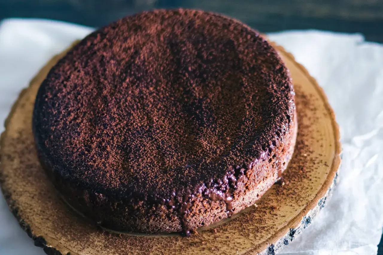En saftig glutenfri chokladkaka, pudrad med kakao och med smält choklad som rinner ner längs kanten.