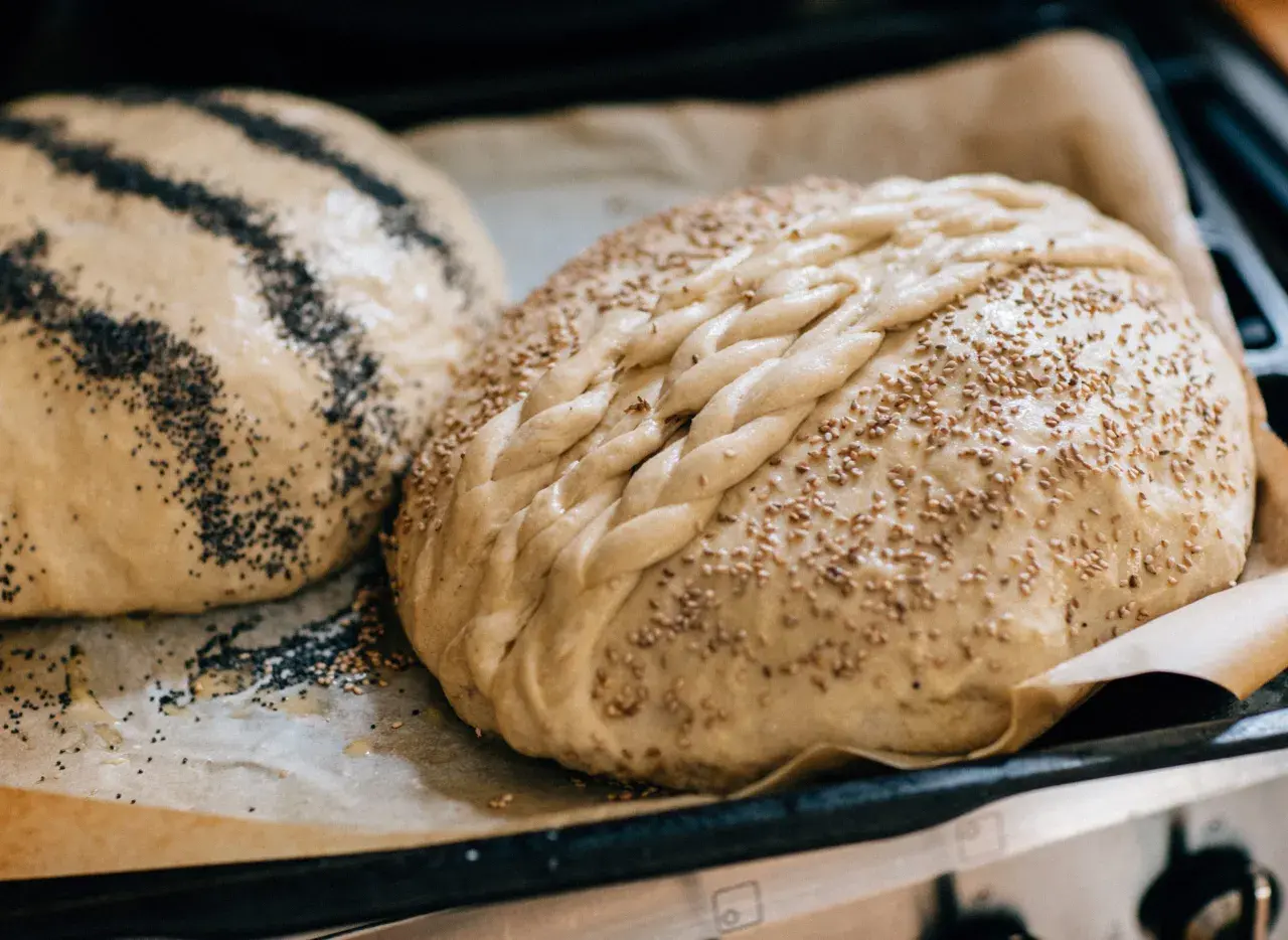 Två hembakade bröd, ett med vallmofrön och ett flätat med sesamfrön, redo att baka och frysa in.