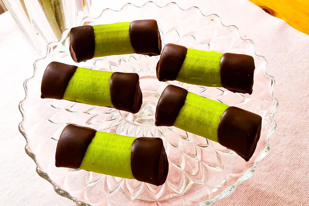 Fem gröna punschrullar med chokladtoppar på ett glasfat. Perfekt för ett enkelt punschrulle recept.
