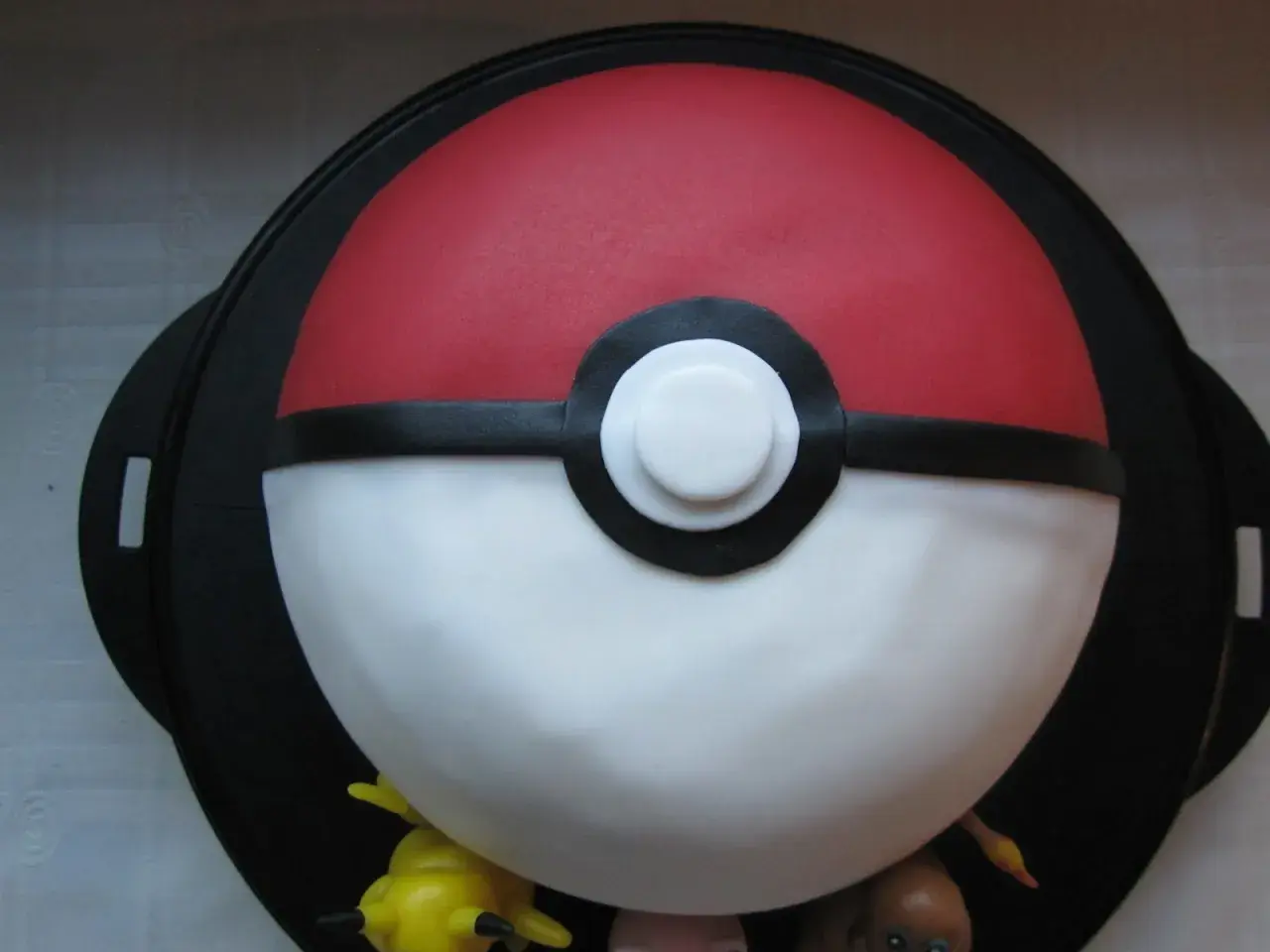En fantastisk pokemon tårta formad som en pokéboll, med små pokemonfigurer som tittar fram.