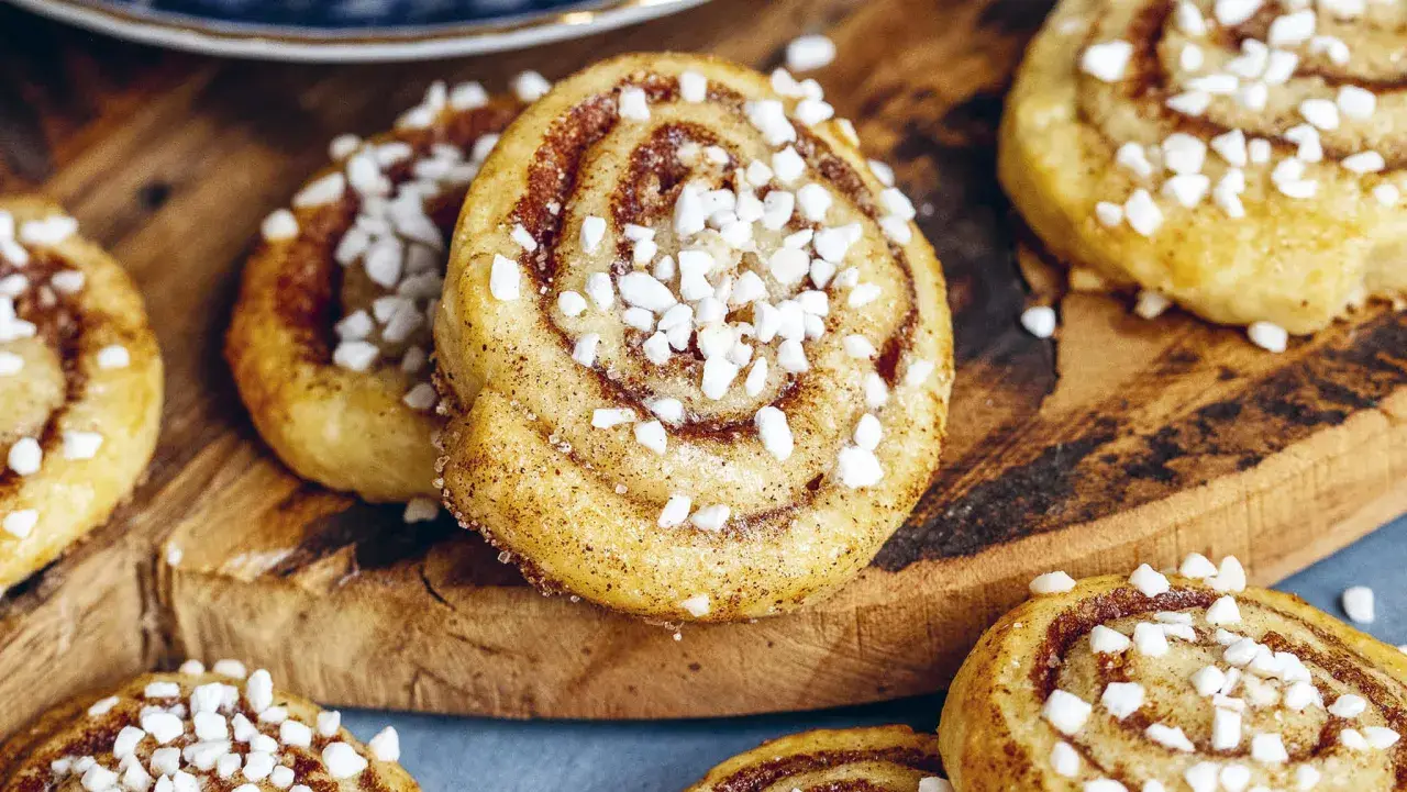 Nybakade kanelbulle kakor med pärlsocker på en träskärbräda. Perfekt fika!