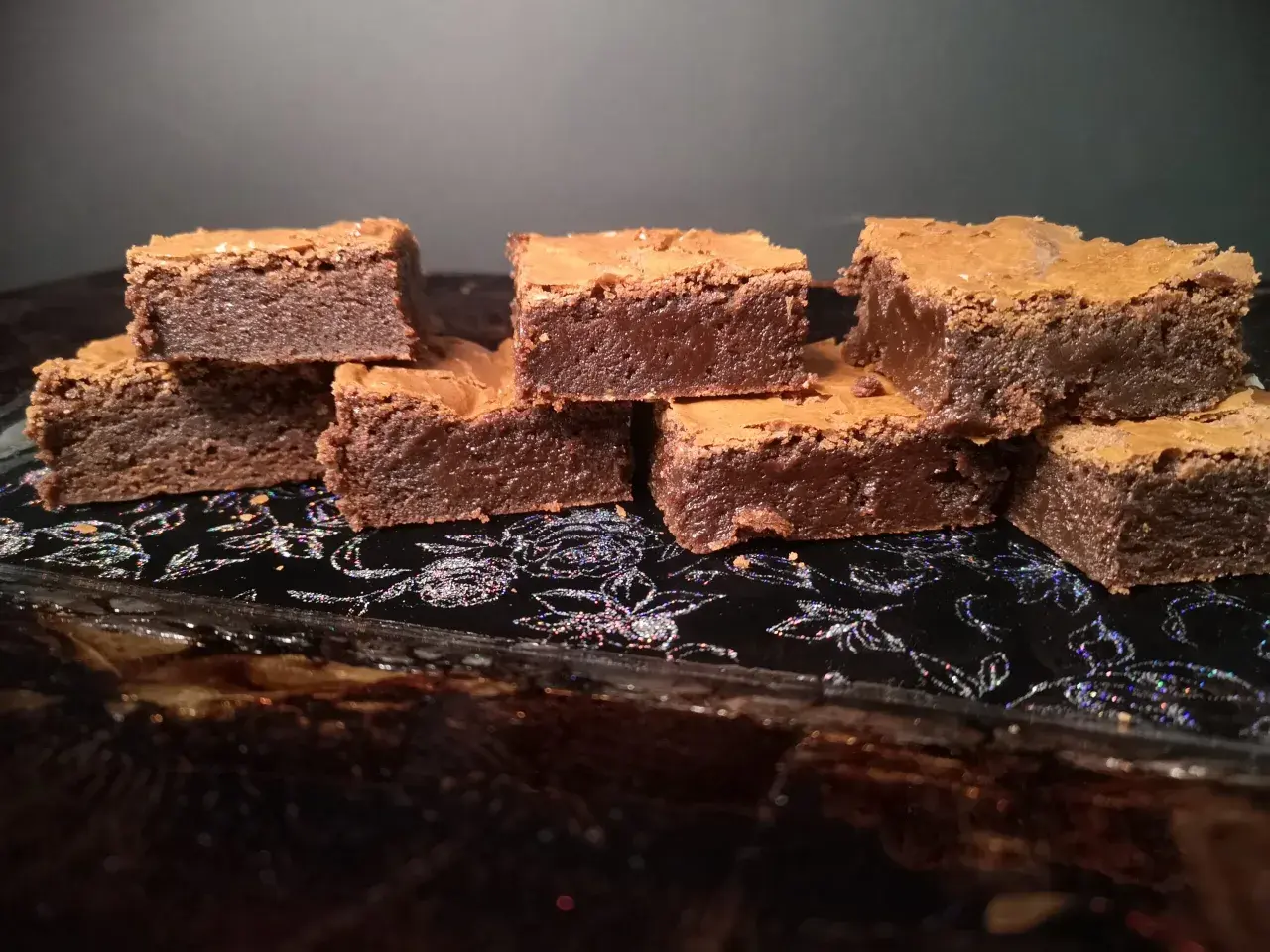 En hög med saftiga chokladbrownies på en glittrig svart bricka. Perfekt för en fika!
