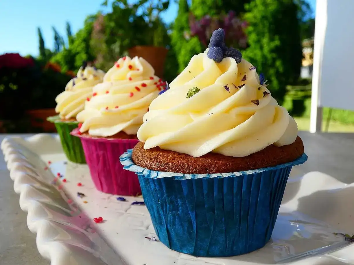 Tre vackra cupcakes med fluffig frosting, perfekta för ett somrigt cupcakes recept. Dekorerade med lila blommor och strössel.