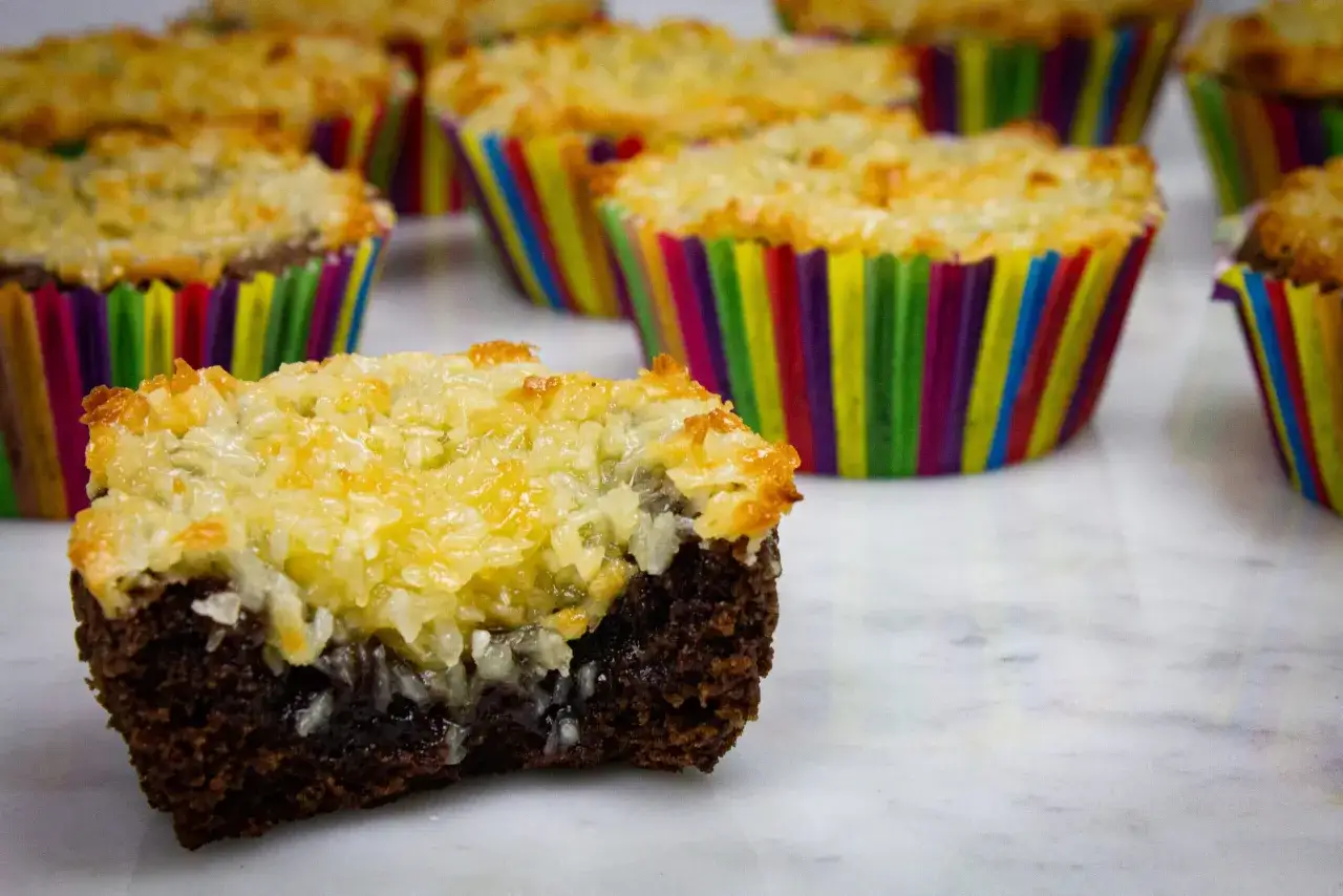 Kladdkakemuffins med tosca-topping i f&auml;rgglada muffinsformar. En muffin &auml;r uppskuren och visar den kladdiga chokladkakan.