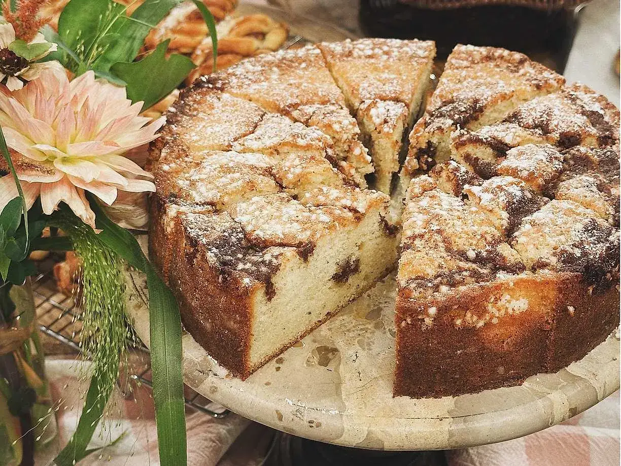 En saftig kanelbulle kaka, pudrad med florsocker, skuren i bitar. Bredvid st&aring;r en vacker bukett blommor.
