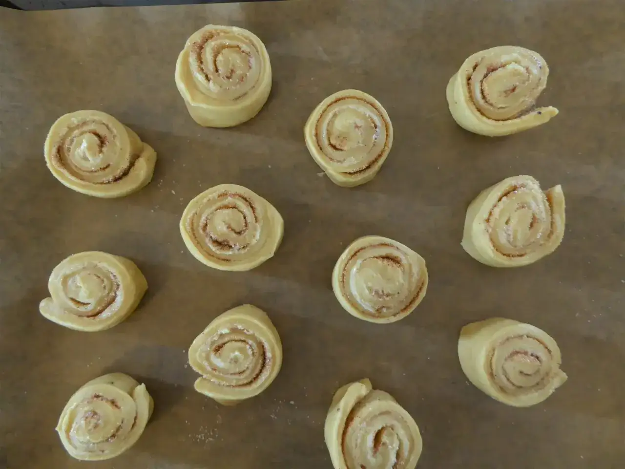 Elva kanelbullar, redo att j&auml;sa med snabbj&auml;st, ligger p&aring; ett bakpl&aring;tspapper.