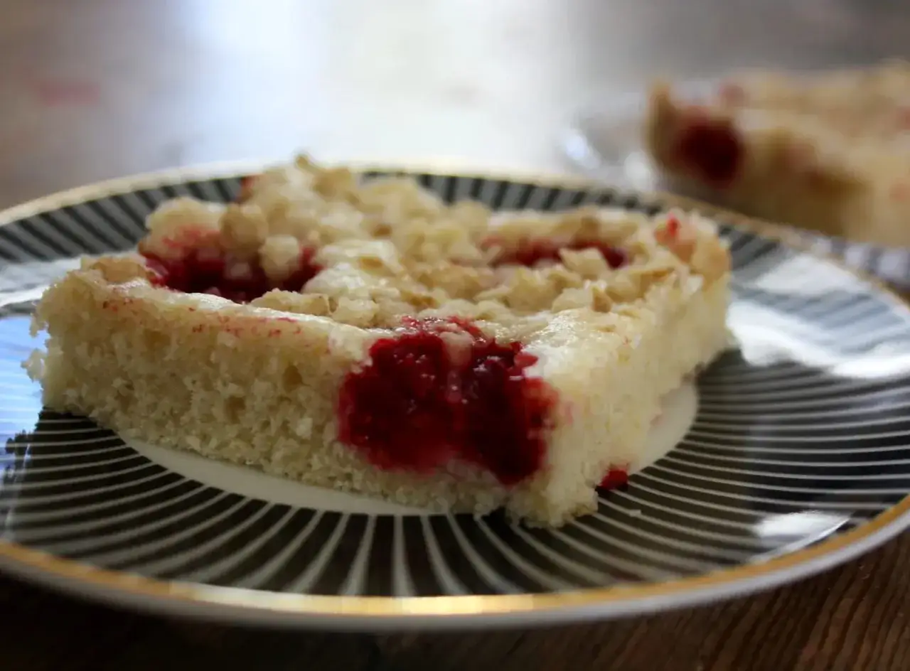 En bit kladdkaka i l&aring;ngpanna med hallon och smuldeg p&aring; en fin tallrik.