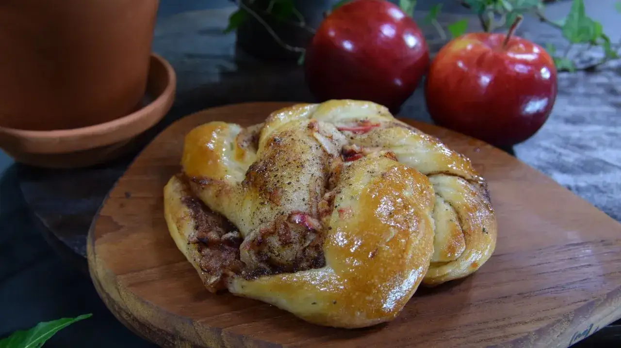 En vackert fl&auml;tad kanelbulle med &auml;pple, perfekt bakad med torrj&auml;st. Tv&aring; r&ouml;da &auml;pplen och en terrakottakruka i bakgrunden.
