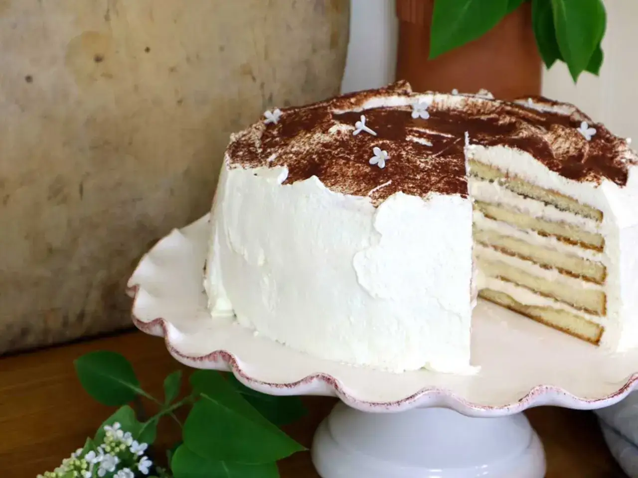 En vacker tiramisu t&aring;rta med lager av kr&auml;m och kex, toppad med kakao och sm&aring; vita blommor.