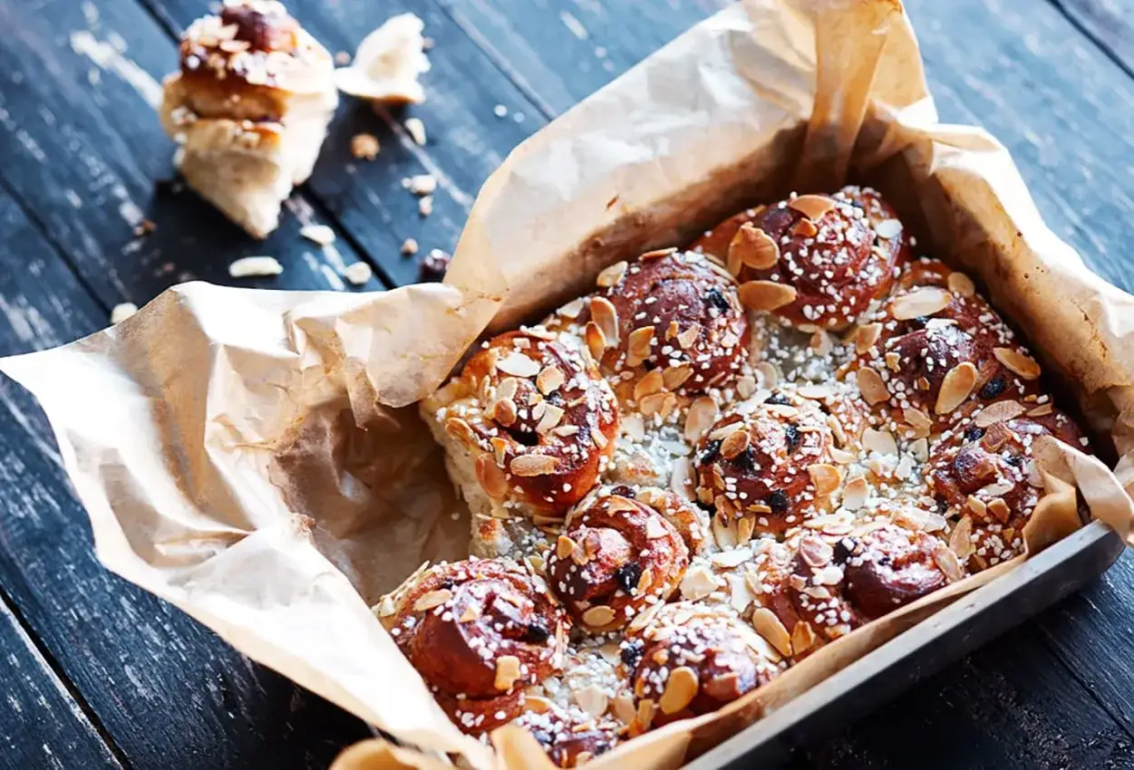En form med nybakade, gyllene snabba butterkakor toppade med mandel och pärlsocker. En ensam bulle ligger bredvid.