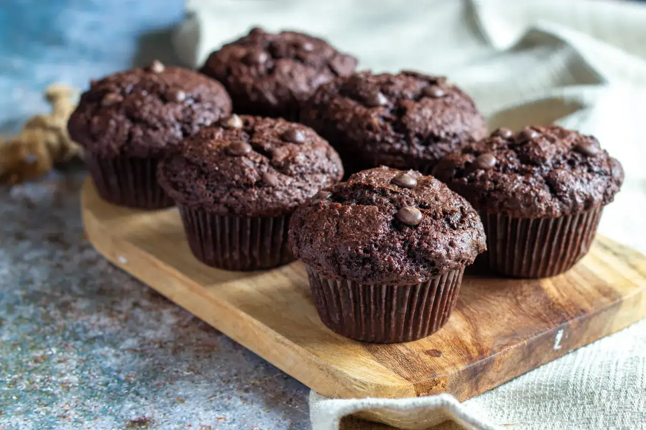 Mörka, saftiga chokladmuffins med chokladknappar, uppradade på en träbricka. Perfekt för fikat!